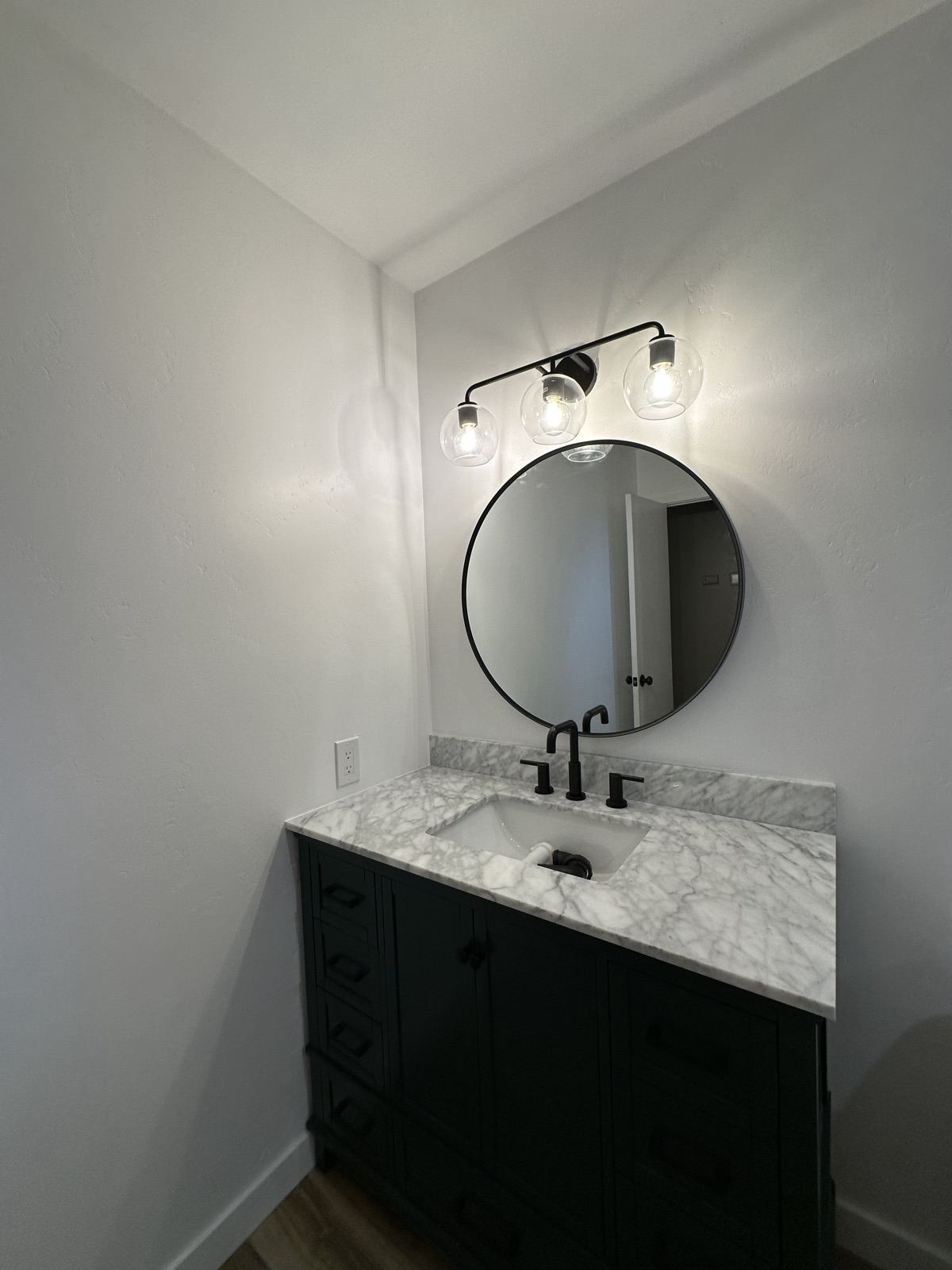 Green vanity with marble countertop, round mirror, and black sconce in the Lakeside bathroom remodel